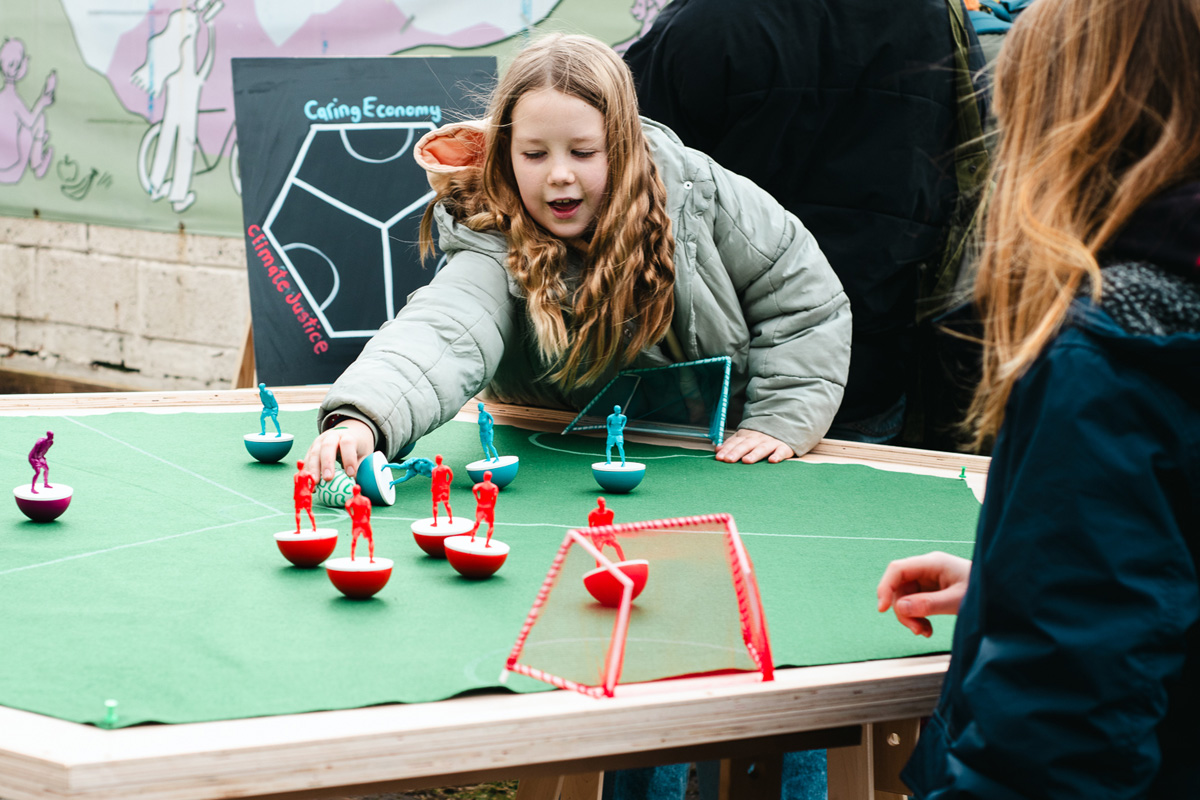 people playing feminist tabletop football with subbuteo-style women and non-binary 3d printed footballers on green felt