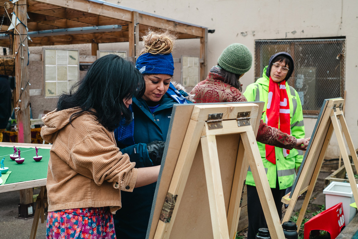 people playing feminist tabletop football with subbuteo-style women and non-binary 3d printed footballers on green felt