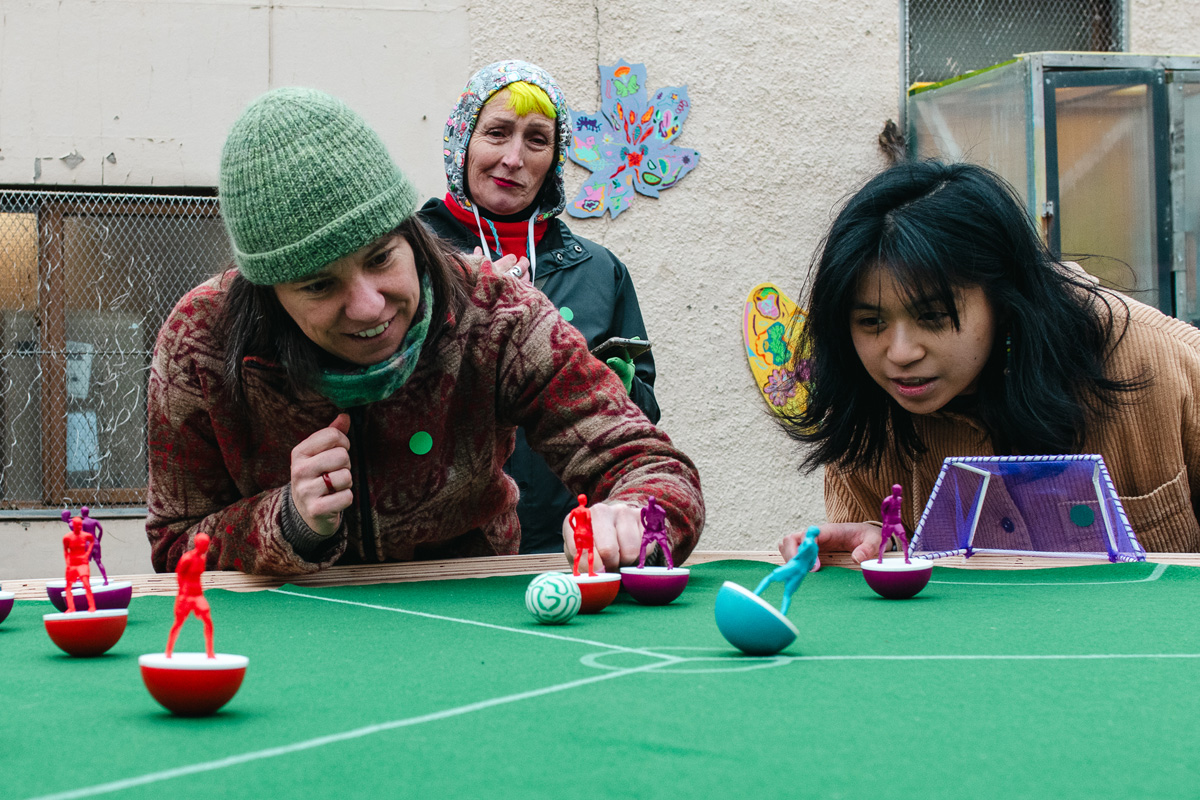 people playing feminist tabletop football with subbuteo-style women and non-binary 3d printed footballers on green felt
